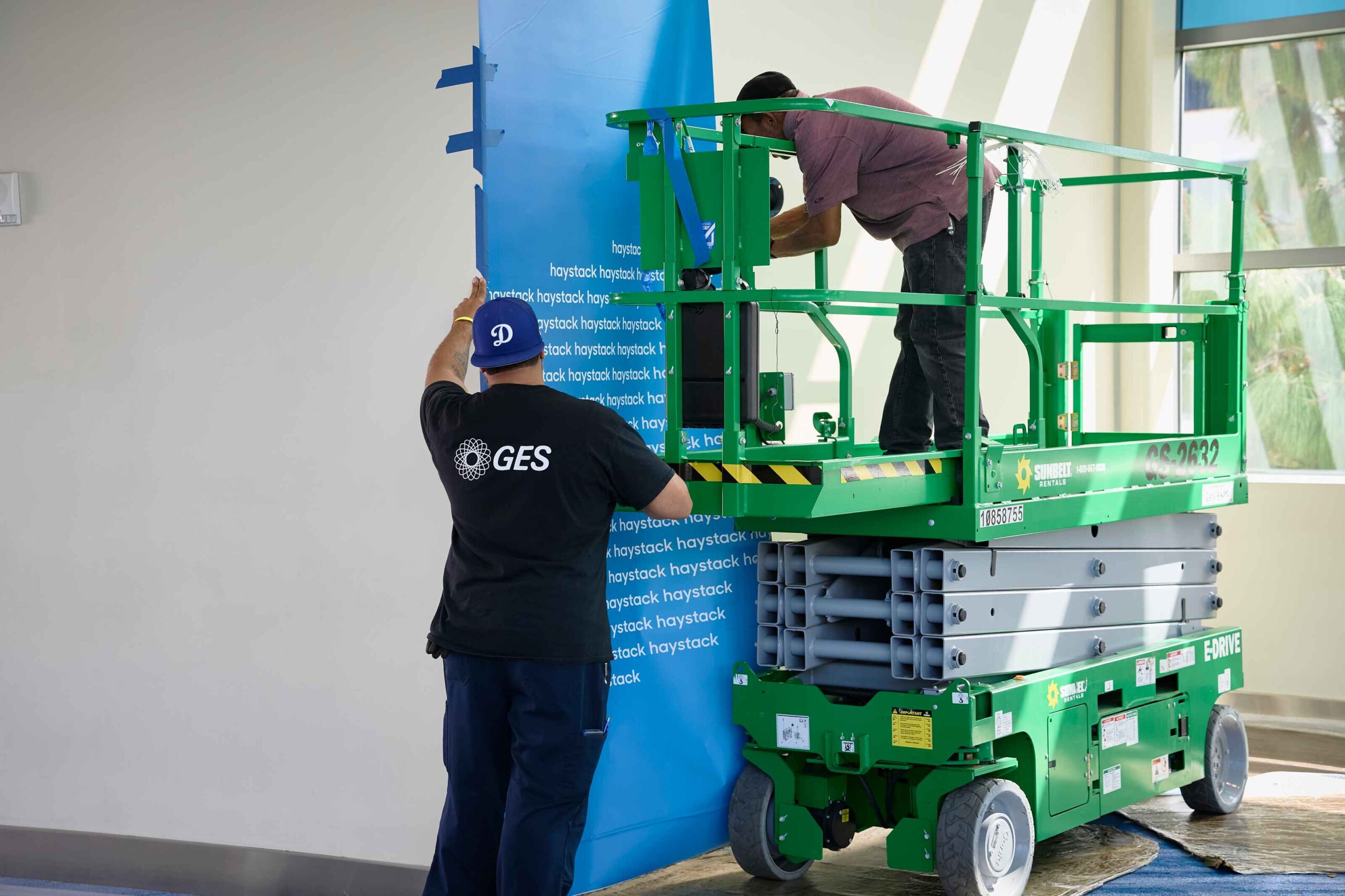 El equipo de GES trabaja en el montaje de los elementos gráficos de la feria desde una plataforma elevadora.